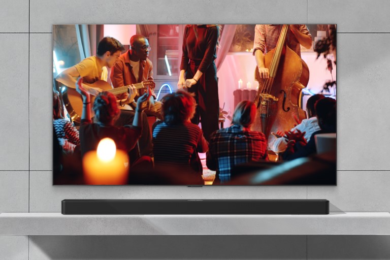 Un concert confortable dans un salon est diffusé sur l’écran. Le menu de l’interface WOW apparaît en surimpression et l’utilisateur navigue vers les paramètres de la barre de son avec la Télécommande Magic. 