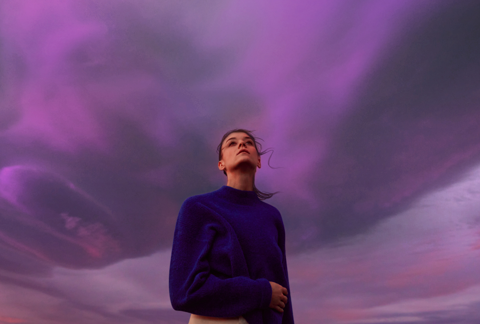 Une femme regarde le ciel violet. Ses cheveux bougent légèrement.