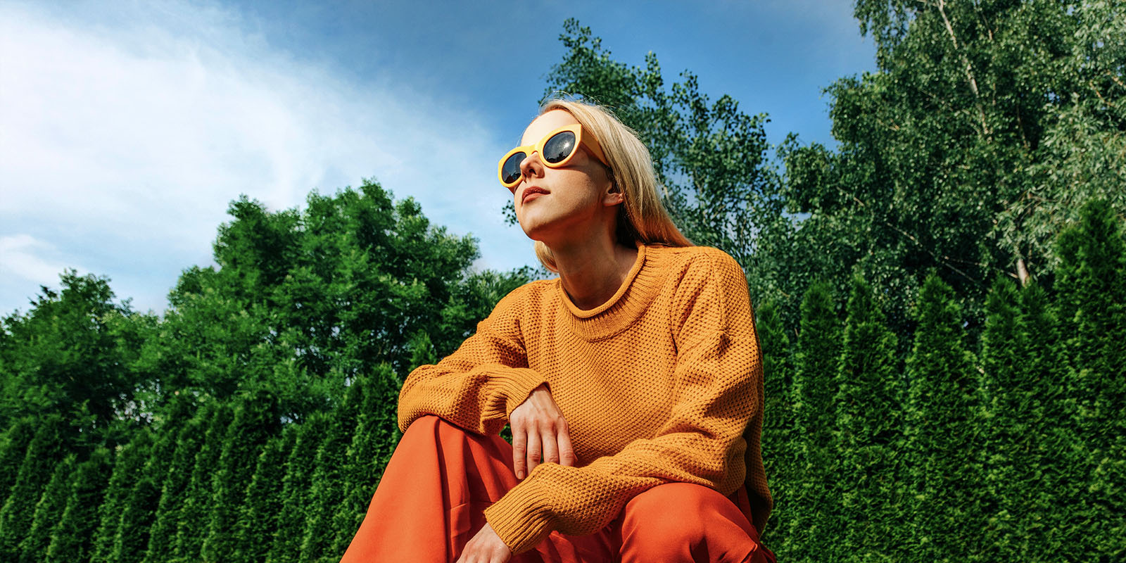 Femme accroupie à l'extérieur par une journée ensoleillée devant des arbres et un ciel bleu dans une cour, image pixelisée. Le mappage tonal et l'effet d'amélioration de l'expression sont appliqués sur la femme, rendant la zone plus lumineuse. L'arrière-plan est ensuite scanné, ce qui le rend plus lumineux.