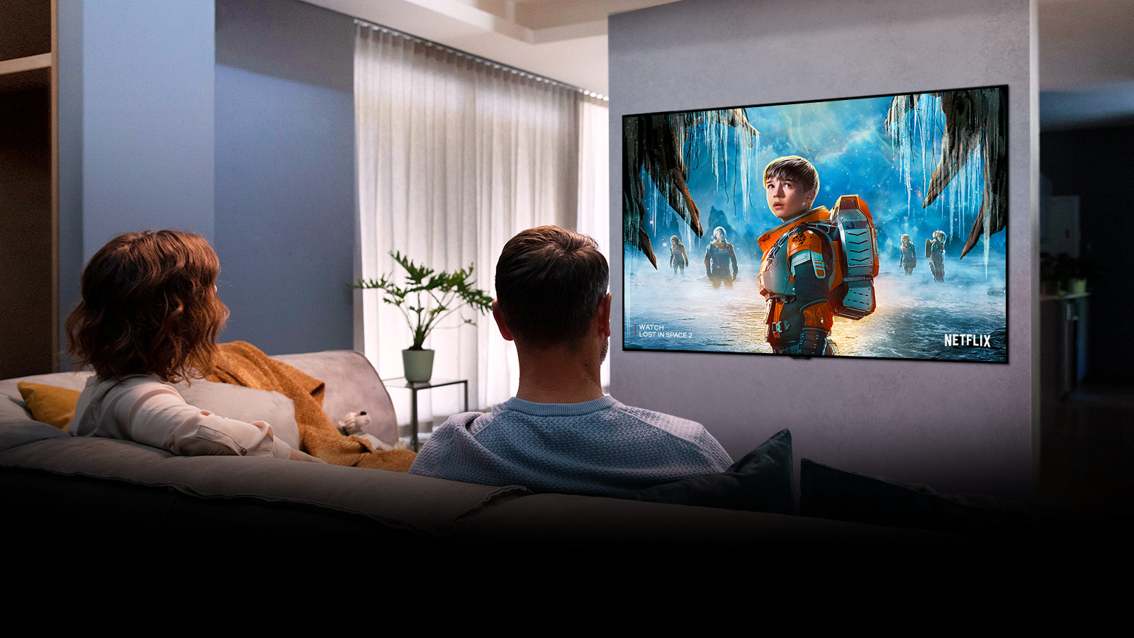 Un couple assis dans un canapé au salon et regardant un film romantique à la télévision