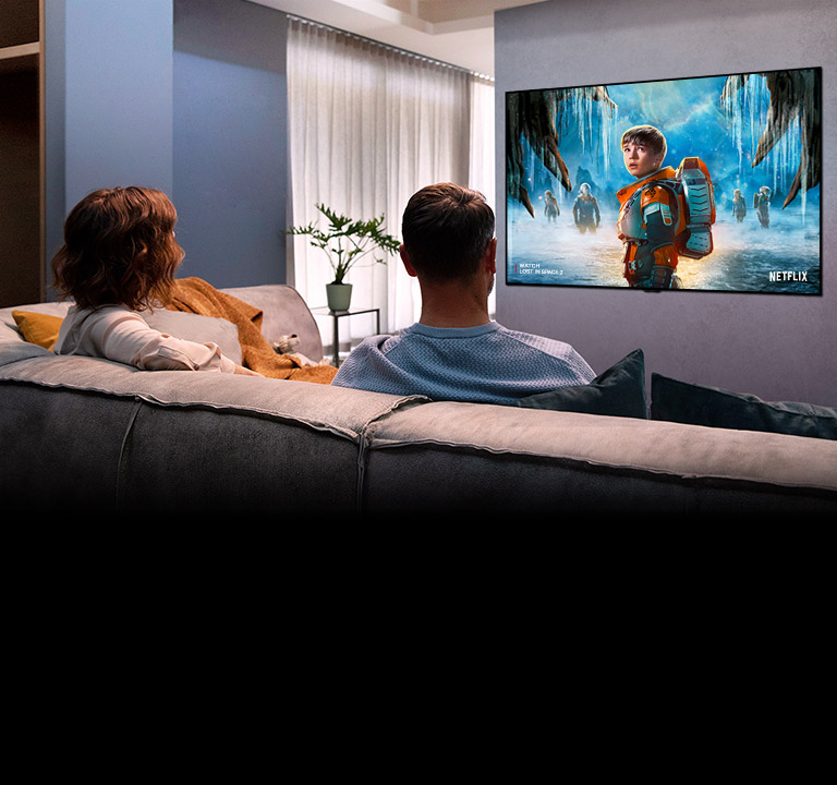 Un couple assis dans un canapé au salon et regardant un film romantique à la télévision