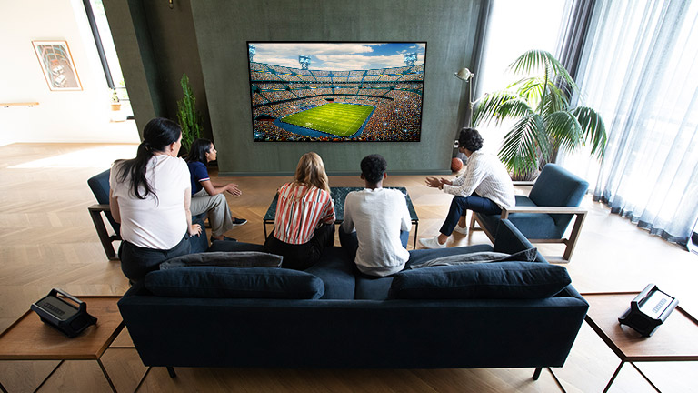 Personnes regardant un jeu de sport sur un téléviseur dans un salon avec des haut-parleurs arrière Bluetooth.