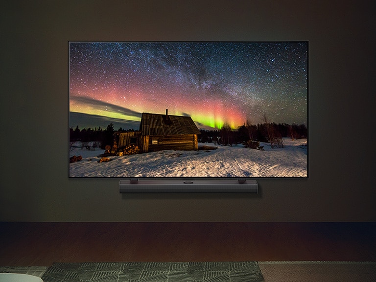 Una imagen de un televisor LG OLED y una barra de sonido LG en un espacio moderno durante la noche. La imagen de la aurora boreal se muestra con los niveles de brillo ideales