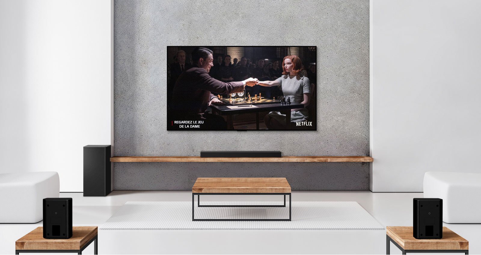 Un ensemble de 2 haut-parleurs arrière, un caisson de basses, une barre de son et un téléviseur se trouvent dans un salon blanc. Une femme et un homme jouent aux échecs sur un écran de télévision. 