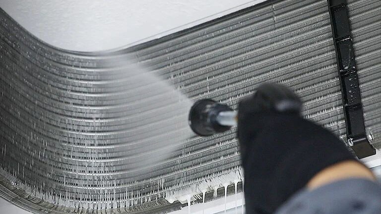 Un homme portant un casque de sécurité couvre avec diligence une unité intérieure ouverte perchée au plafond d'une housse en plastique protectrice.