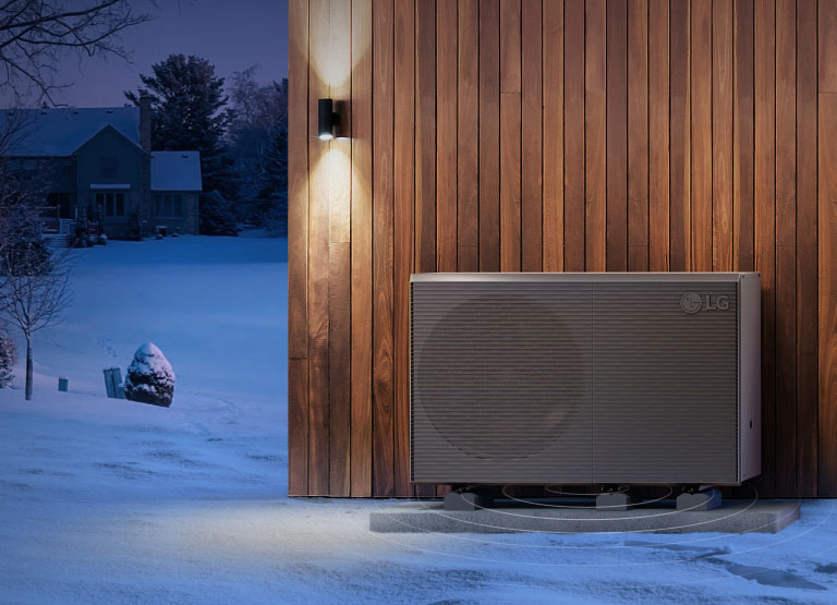 Des pompes à chaleur LG THERMA&nbsp;V sont fixées au mur extérieur d’une maison en bois sur un arrière-plan de villages enneigés.