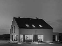 Une unité extérieure entre un mur de briques recouvert de neige et une maison à deux étages équipée de larges fenêtres transparentes donnant sur une salle de séjour.