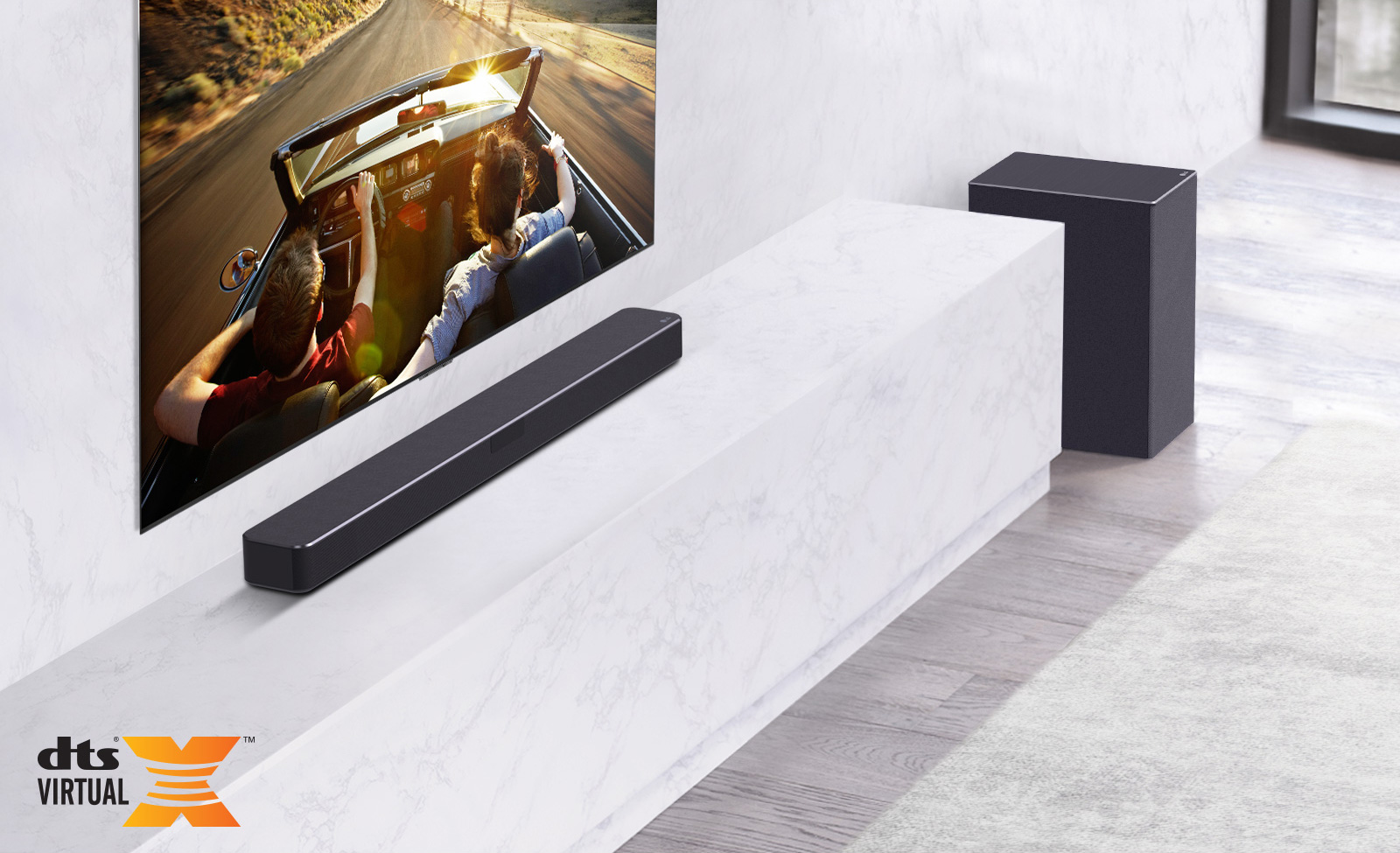 Le téléviseur est au mur, la barre de son LG est en bas sur une étagère en marbre blanc avec un caisson de basses à droite. Le téléviseur montre un couple dans une voiture.