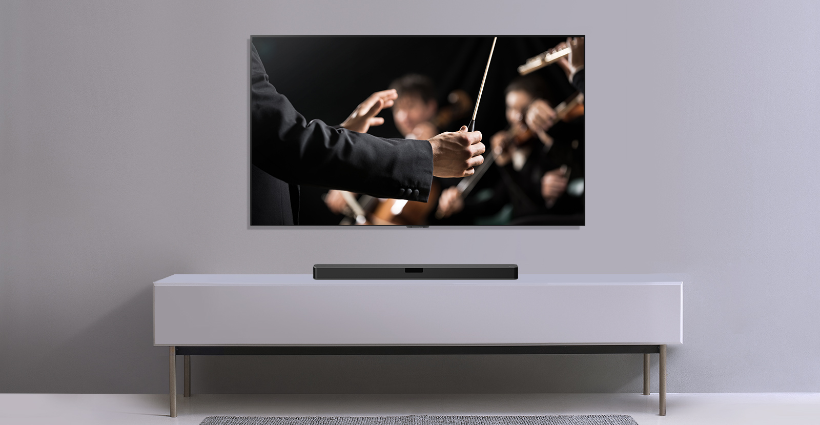 Un téléviseur est représenté sur un mur gris et la barre de son LG en dessous sur une étagère grise. Le téléviseur montre un chef d'orchestre dirigeant un orchestre.