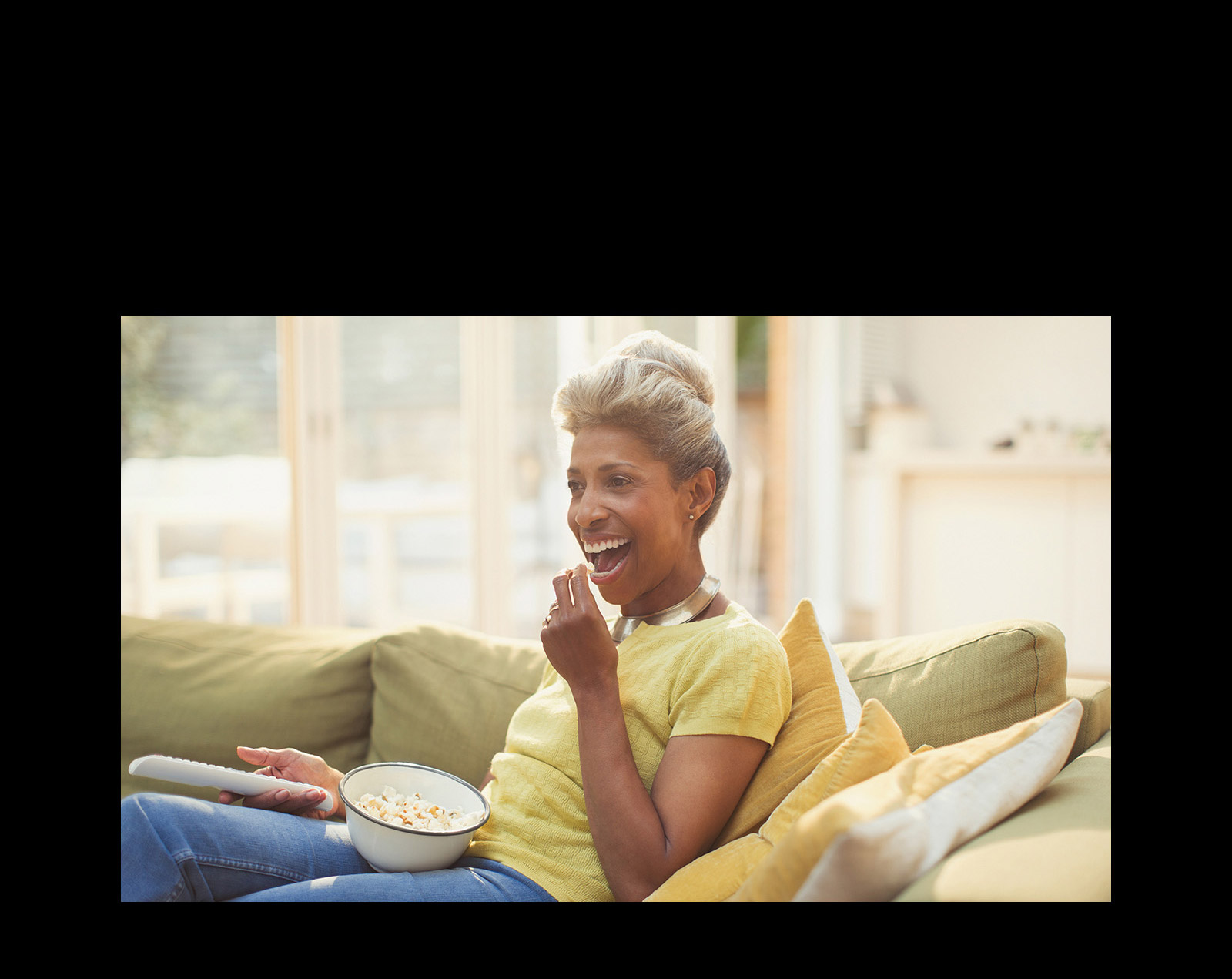 Une femme regarde le téléviseur – tenant une télécommande. Elle mange également du pop-corn.