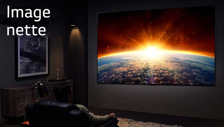 Un homme assis sur un canapé dans une pièce sombre regarde le téléviseur qui affiche le soleil se couchant derrière la Terre.