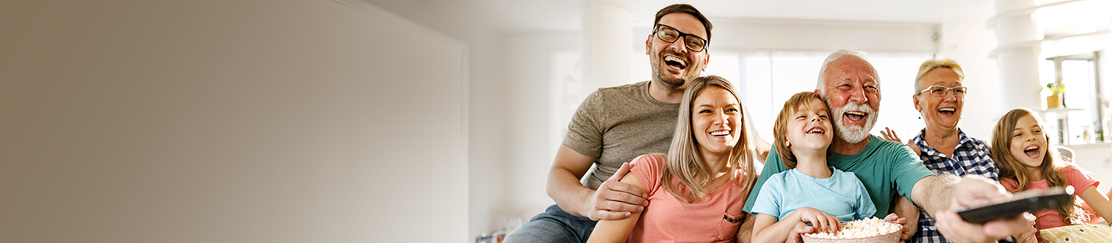 Une famille est assise et rit, tandis que le grand-père dirige la télécommande vers l’extérieur.
