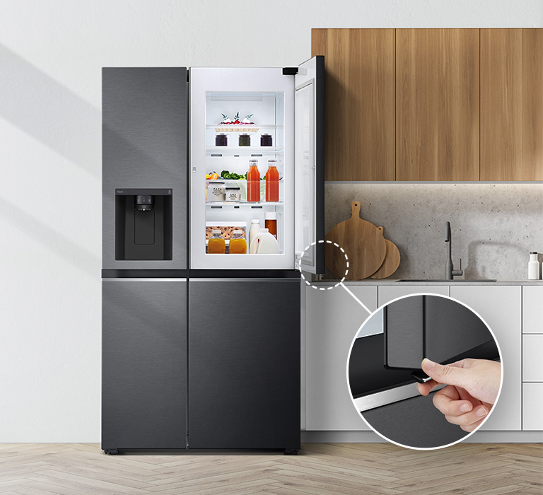 Le réfrigérateur est présenté de face, installé dans une cuisine. La porte supérieure droite est ouverte et un cercle et une ligne mènent vers un cercle de plus grande taille, qui présente un zoom sur le bouton dans le coin inférieur droit de la porte ouverte, qui est dotée d’un bouton d’ouverture caché.