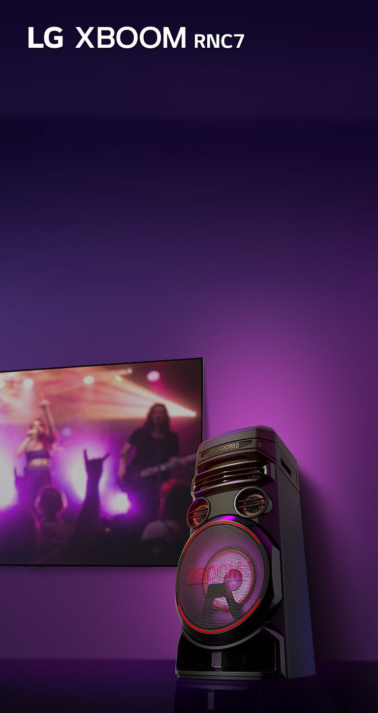 Vue en contreplongée du côté droit de l’enceinte LG XBOOM RNC5 sur fond violet.  L’éclairage du XBOOM est également violet. Et un écran de télévision diffuse un concert.