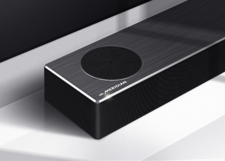 Gros plan de la barre de son LG sur le côté gauche, avec le logo Meridian en bas à gauche. Le côté inférieur gauche du téléviseur est également visible. 