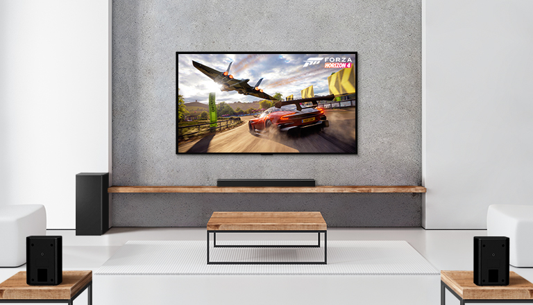 Un ensemble de 2 haut-parleurs arrière, un caisson de basses, une barre de son et un téléviseur se trouvent dans un salon blanc. On peut voir une voiture qui roule et un vaisseau spatial sur l’écran du téléviseur. 