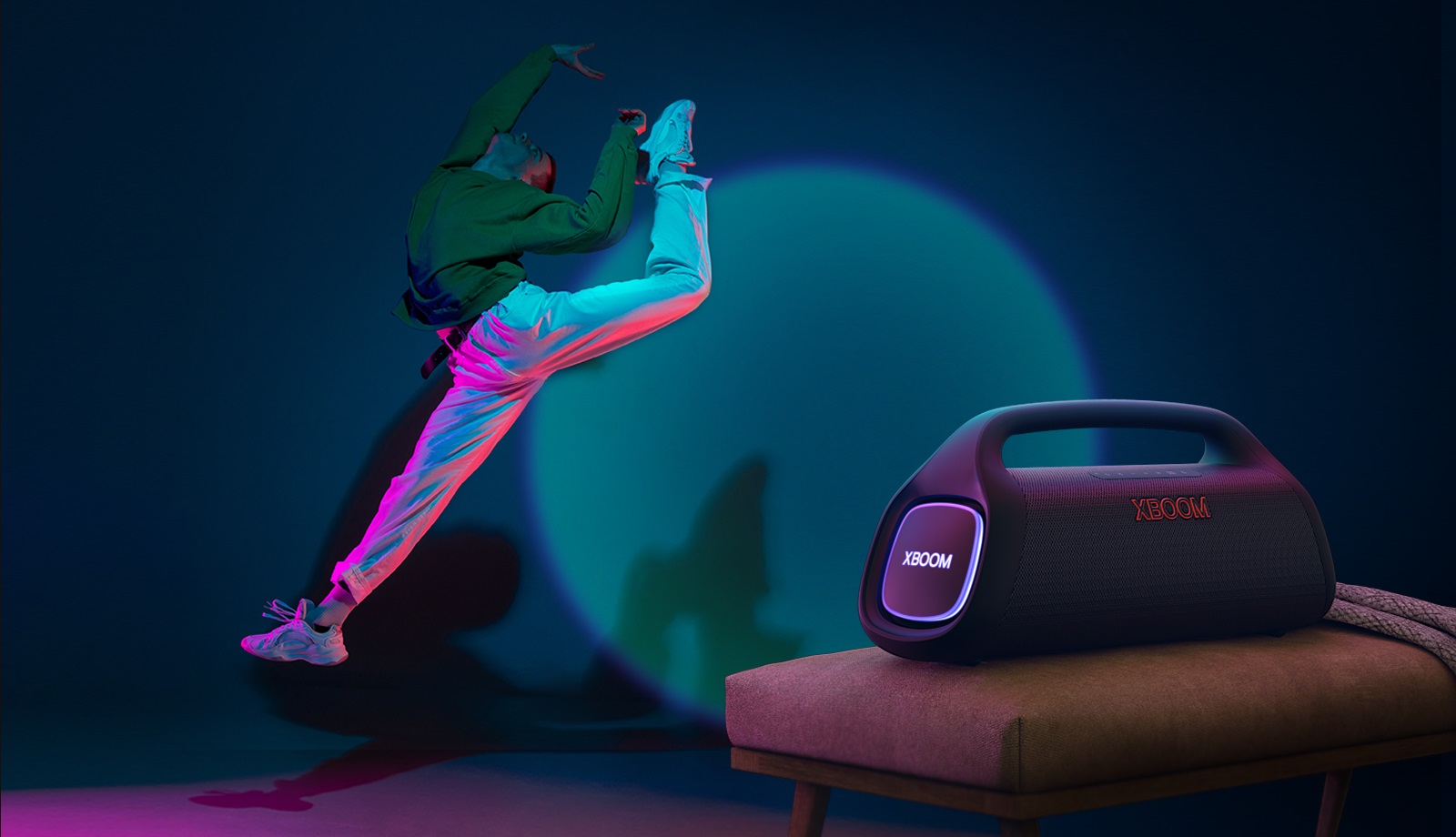 La LG XBOOM Go XG9 est posée sur la chaise. Elle émet une lumière scénique sur le mur et une personne danse devant.