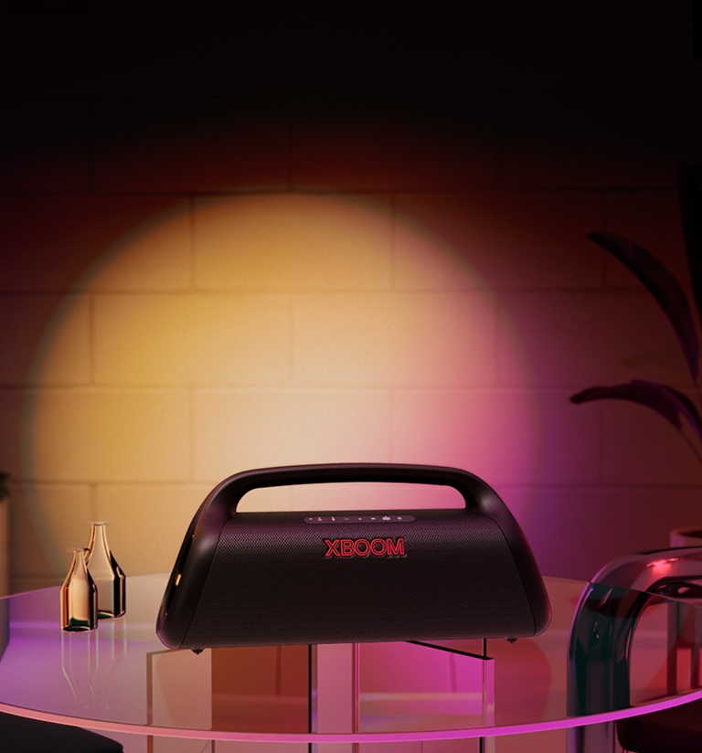 Une image de la LG XBOOM Go XG9. Elle est posée sur la table en verre de la maison et projette un éclairage scénique en dégradé orange et rose.