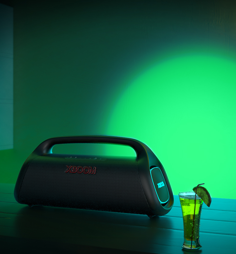 La LG XBOOM GO XG9 est posée sur le comptoir du bar. Elle projette une lumière scénique verte et bleue