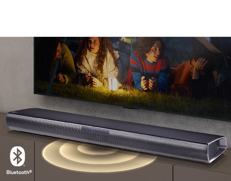 Le téléviseur LG est accroché au mur&nbsp;; l’écran montre 2&nbsp;couples allongés sur l’herbe. Devant eux se trouve une lampe. La barre de son LG se trouve sous le téléviseur LG. Un graphique représentant du son sort de l’avant de la barre de son. Le logo Bluetooth est visible dans le coin inférieur gauche de l’image.