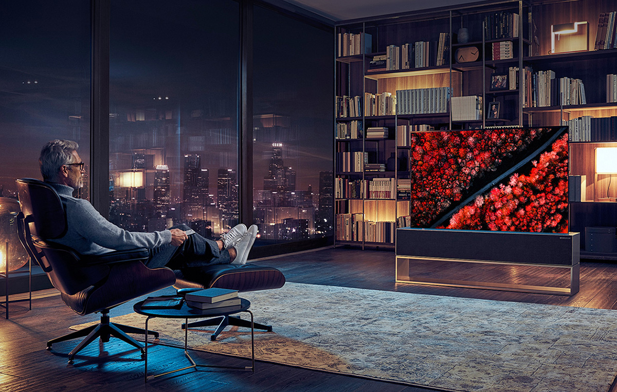Un homme est assis sur un fauteuil inclinable, les jambes croisées et son corps est tourné vers le téléviseur OLED enroulable LG SIGNATURE.
