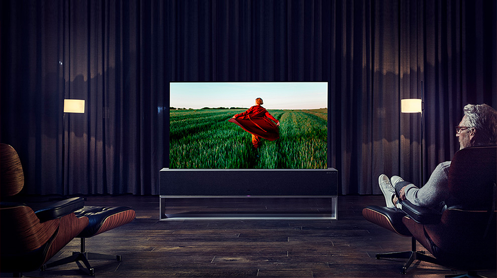 Un homme est assis sur un fauteuil inclinable, les jambes croisées et son corps est tourné vers le téléviseur OLED enroulable LG SIGNATURE.
