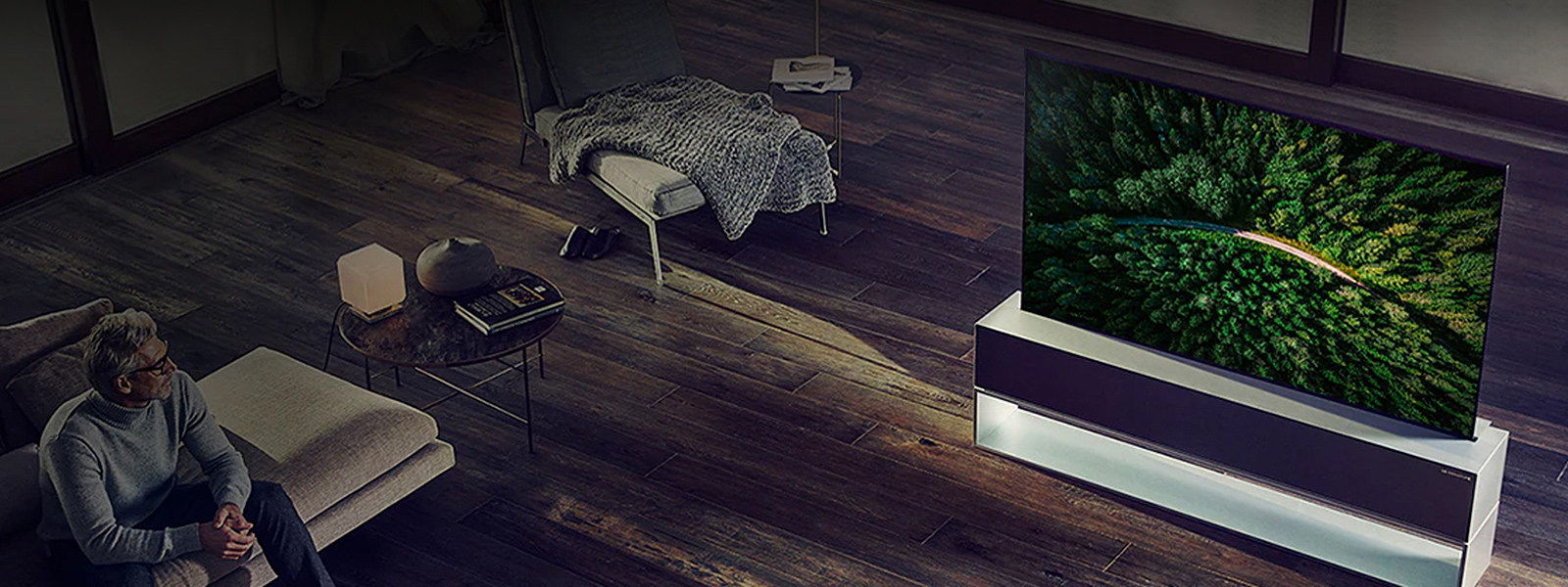 Le téléviseur OLED enroulable LG SIGNATURE est placé sur le parquet du salon de luxe et un homme regarde la télévision.