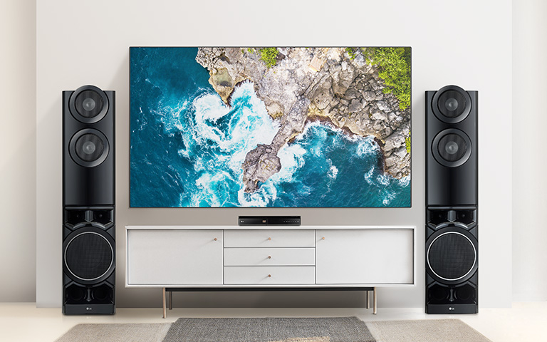 Entre les deux haut-parleurs, la TV est sur un mur et la table est sous le lecteur DVD. Le téléviseur montre des vagues qui échouent sur des rochers.