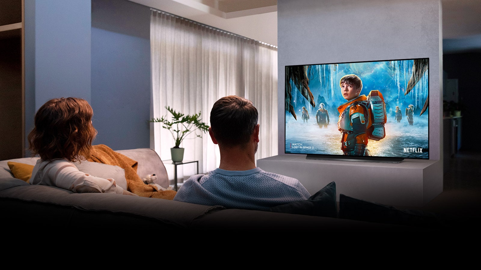 Couple sitting on a sofa in the living room watching a romantic movie on TV