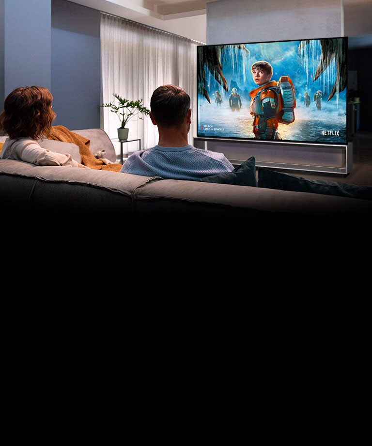 Couple sitting on a sofa in the living room watching a romantic movie on TV