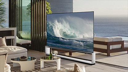 Le LG OLED Z2 se trouve dans une pièce blanche minimaliste, devant une fenêtre qui s’ouvre sur une forêt d’arbres