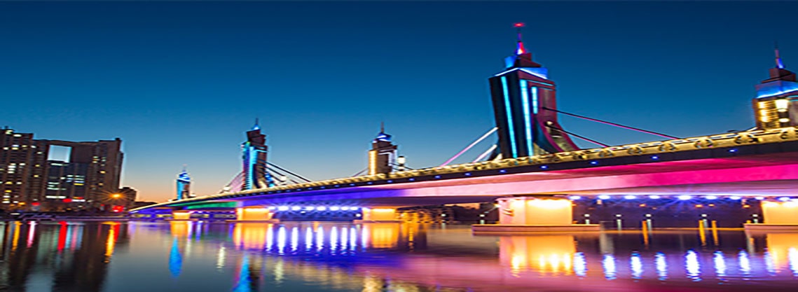 Vista nocturna de un puente iluminado con rascacielos de fondo y luces vívidas reflejadas en el agua, para demostrar el alto contraste y el detalle del color.