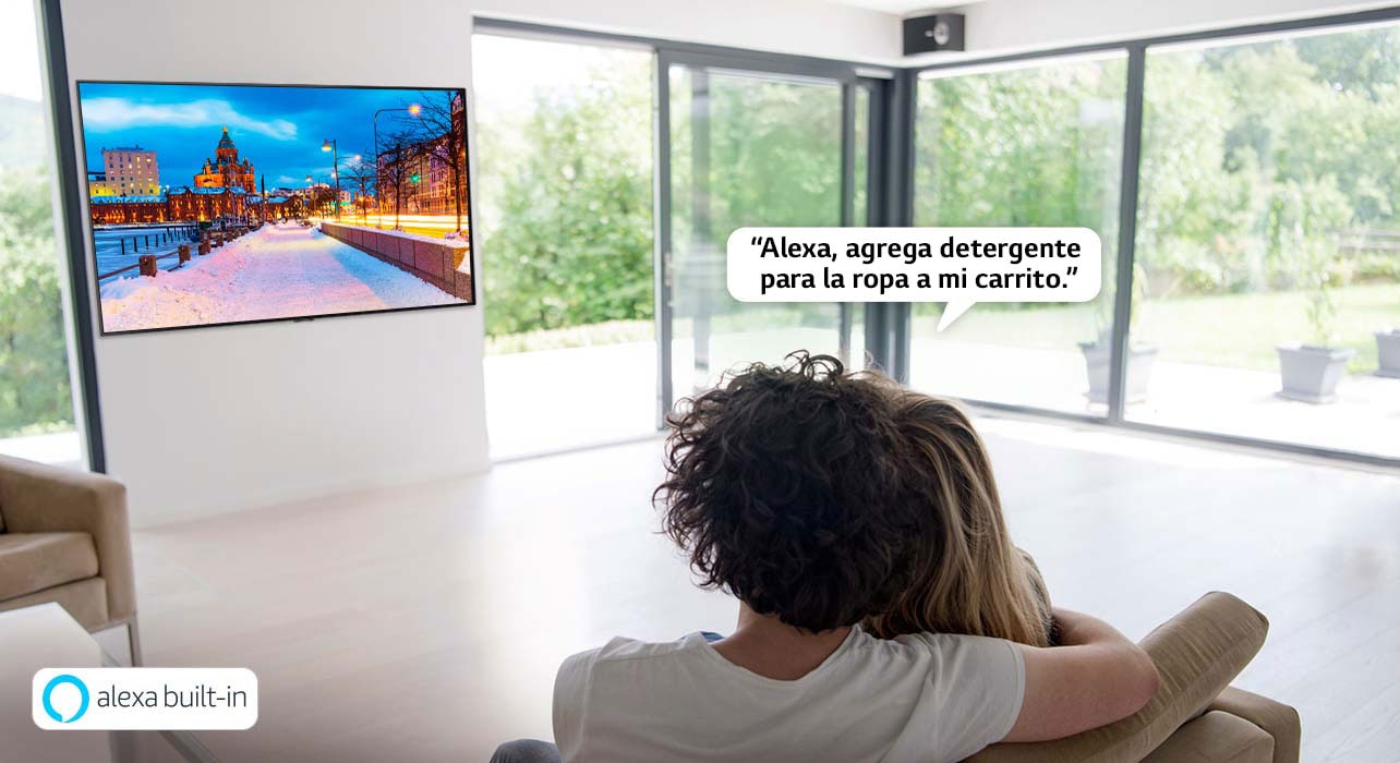 Pareja sentada en un sofá pidiéndole a Amazon Alexa que agregue detergente para la ropa al carrito de compras