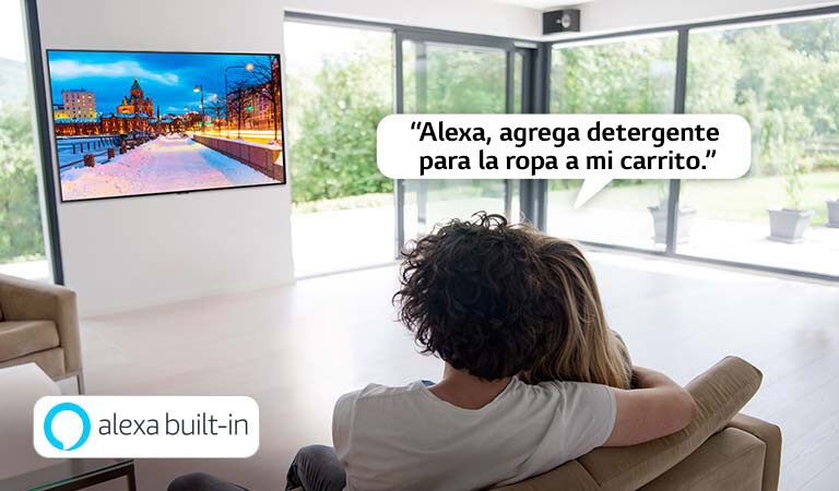 Pareja sentada en un sofá pidiéndole a Amazon Alexa que agregue detergente para la ropa al carrito de compras