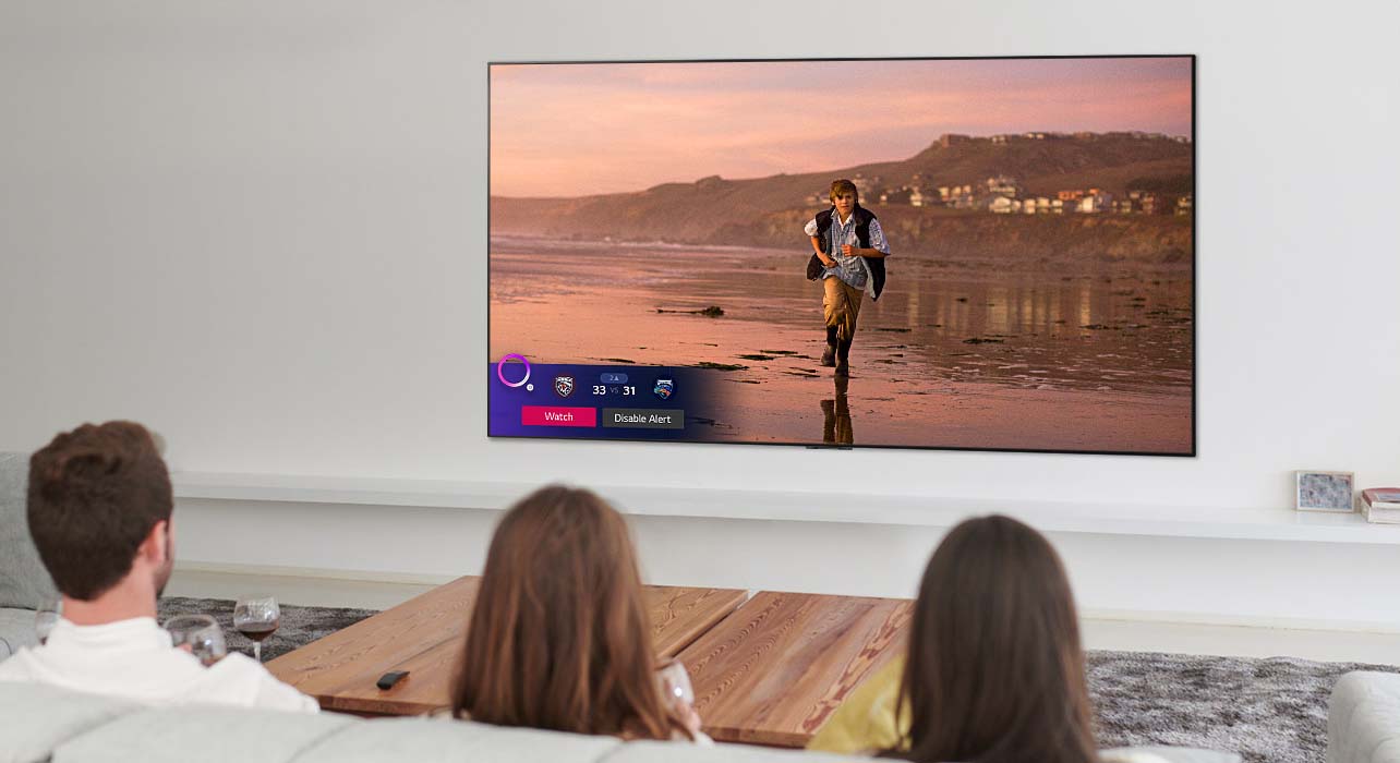 Tres personas mirando la pantalla de TV que muestra una escena de una película de fantasía con un Alerta de deportes