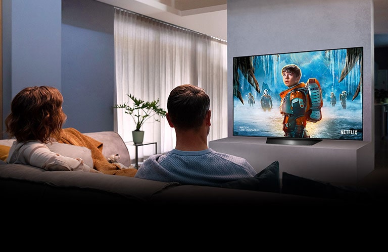 Pareja sentada en un sofá en la sala viendo una película romántica en la televisión