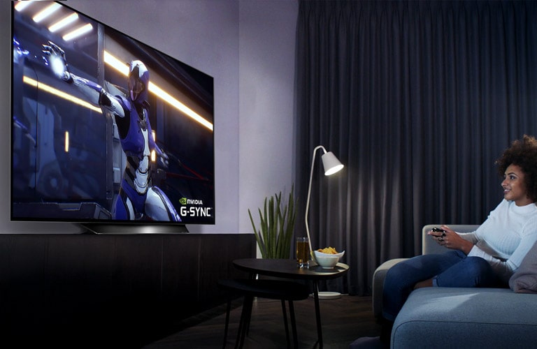 Hombre sentado en una silla de juego de carreras, sosteniendo un volante mientras juega un juego de carreras en una pantalla de TV