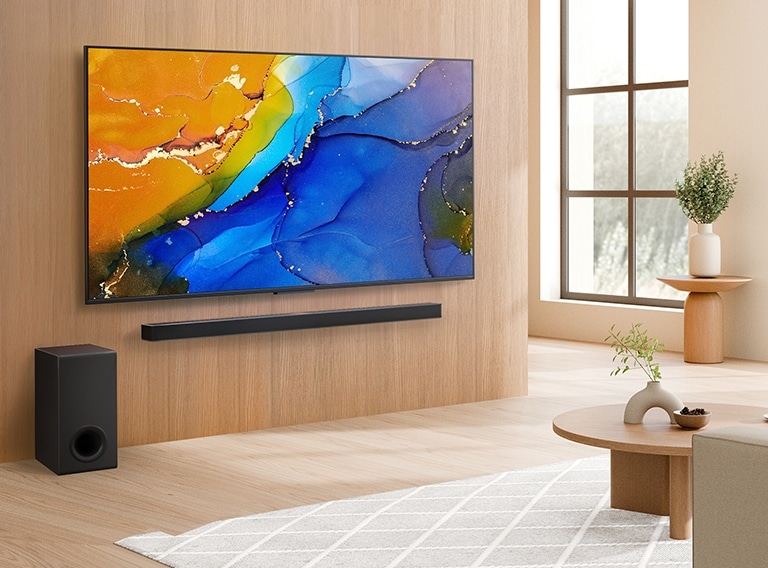 La LG QNED TV montada en una pared sobre una LG Soundbar en una sala de estar moderna. La LG QNED TV muestra un fondo colorido y abstracto.