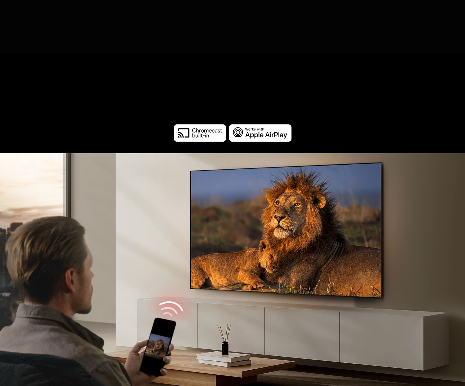  Un televisor LG montado en la pared de una sala de estar, que muestra un león y un cachorro de león. Un hombre se sienta en primer plano con un teléfono inteligente en la mano que muestra la misma imagen de leones. Un gráfico de tres barras curvas de color rojo neón se muestra justo encima del teléfono inteligente que apunta hacia el televisor.