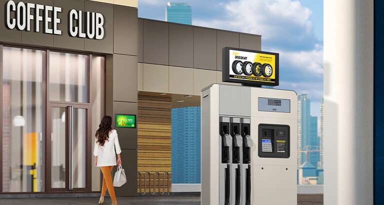 Los anuncios de neumáticos se muestran en un 22XE1J instalado en la parte superior del lubricador de gas. Una señora que entra en un café mira el anuncio del 22XE1J que está instalado en la pared del edificio.