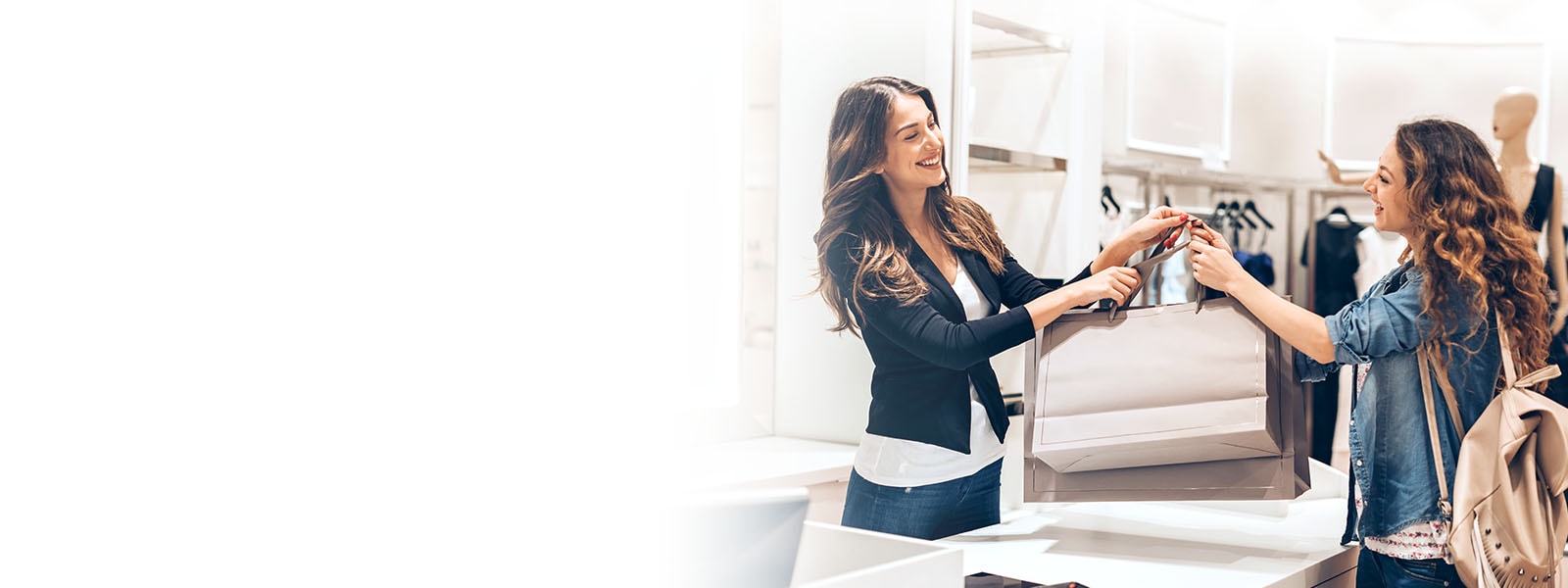 An Image of a sales clerk smiling and giving a customer shopping bags in a clothing store.