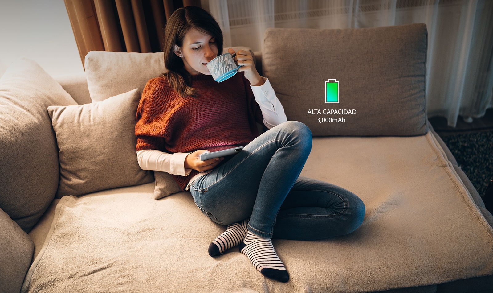 Mujer sentada en un sofá tomando café y mirando su teléfono inteligente