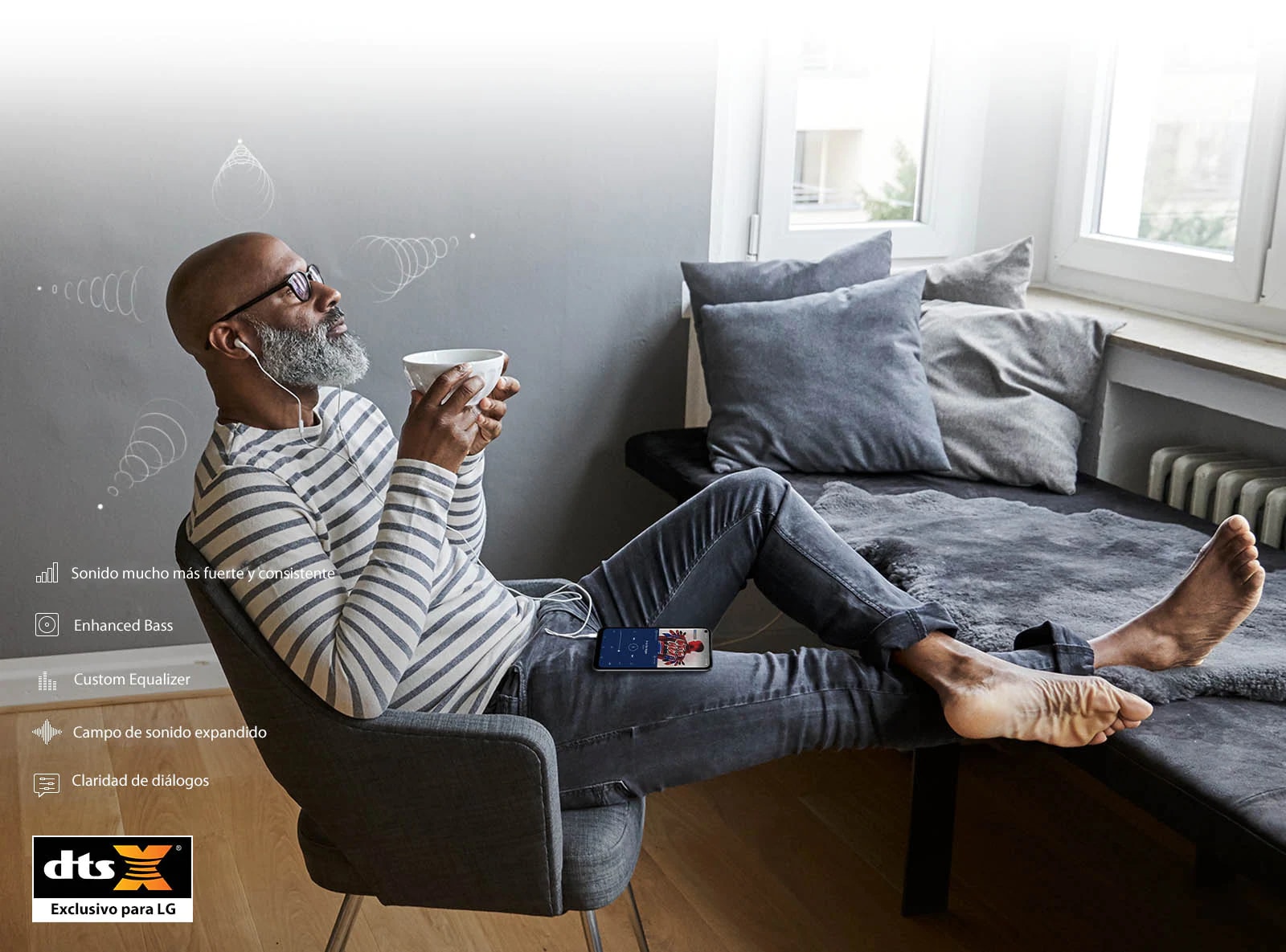 Man sitting in a chair drinking coffee and listening to music through his earphones
