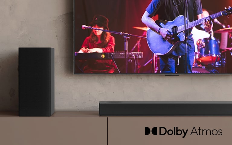 El televisor LG muestra un concierto y la barra de sonido LG se coloca debajo del televisor LG. A la izquierda, el altavoz trasero está en el estante marrón.