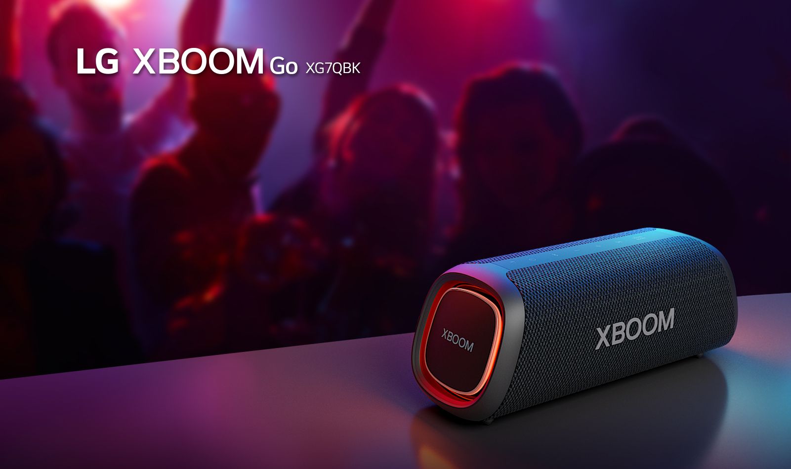 LG XBOOM Go XG7 está colocado sobre la mesa de metal con una luz naranja encendida. Detrás de la mesa, la gente disfruta de la música.