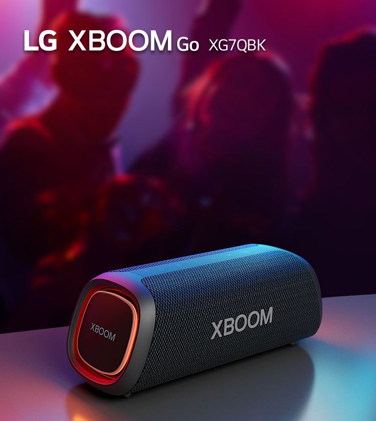 LG XBOOM Go XG7 está colocado sobre la mesa de metal con una luz naranja encendida. Detrás de la mesa, la gente disfruta de la música.