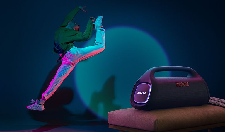 LG XBOOM Go XG9 se coloca en la silla. Proyecta una iluminación escénica en la pared y una persona baila frente a ella.