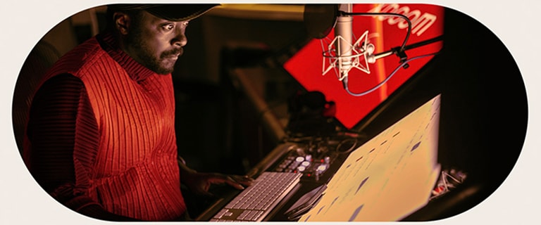 will.i.am está trabajando en el estudio, mirando una pantalla colocada debajo de un micrófono.
