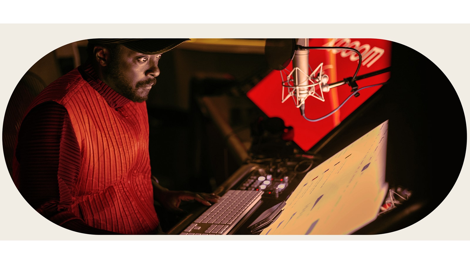 will.i.am está trabajando en el estudio, mirando una pantalla colocada debajo de un micrófono.