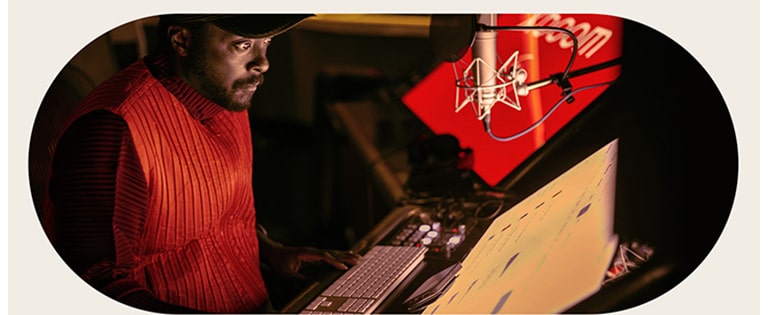 will.i.am está trabajando en el estudio, mirando una pantalla colocada debajo de un micrófono.